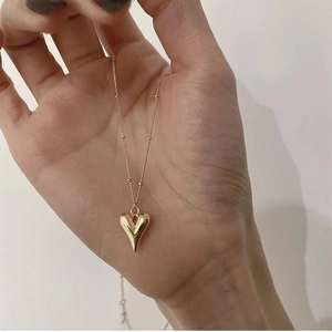 3D golden heart pendant necklace with beaded satellite chain shown in a hand closeup