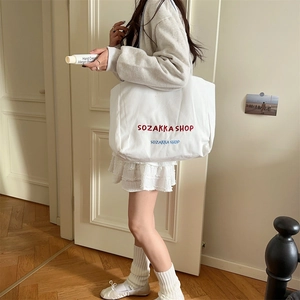 Detailansicht des weißen Canvas-Shoppers mit gestickten Buchstaben und langen Trägern