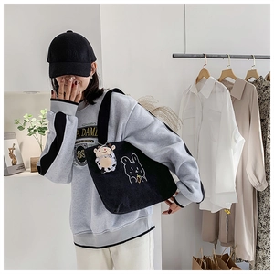Detail of black corduroy tote bag with rabbit embroidery and cow plush keychain