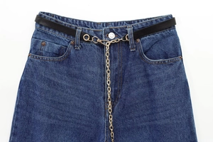 Dettaglio dei jeans blu scuro con cintura in pelle sottile e catena in metallo dorato