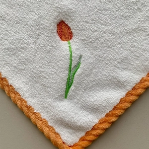 Detailed close-up of white coral fleece towel with orange tulip embroidery and thick hem