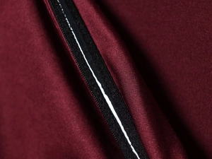 Makroaufnahme von dunkelrotem Strickstoff mit schwarzem Zierstreifen und weißem Reflexstreifen
