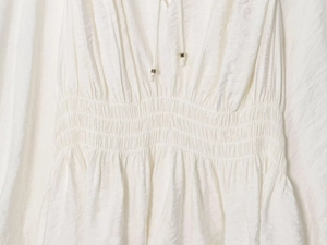 Detailed macro view of white pleated fabric featuring drawstring neckline and elastic waist