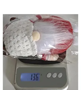 Détail d'un gnome de Noël en peluche affichant un poids de 136 grammes sur une balance