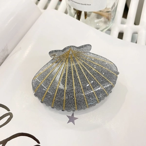 Pince à cheveux coquillage gris pailleté avec lignes dorées et strass sur un magazine