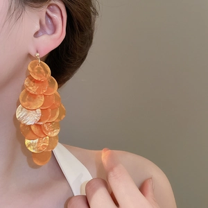 Detail shot of long tiered earrings with orange shell discs and golden metallic pins