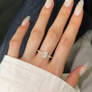Close-up of golden ring with emerald-cut zirconia stone and pavé diamond setting