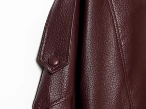 Gros plan sur le bouton et la texture grainée de la veste en cuir PU bordeaux
