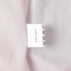 Macro shot of white laundry care label showing 100% cotton fabric and washing icons