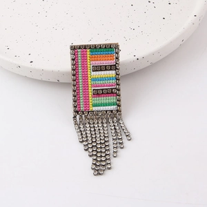 Detail of colorful woven brooch with rhinestone fringe and crystal border on white tray