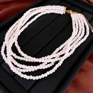 Collier élégant à cinq rangs de perles blanches avec fermoir doré sur fond rouge