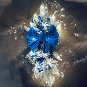 Close-up of snowy Christmas swag with blue velvet bow, pinecones, and warm LED lights