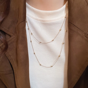 Detail of layered gold beaded necklace on a model with minimalist metal rice beads