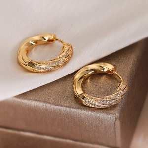 Close-up of twisted gold hoop earrings with sparkling cubic zirconia on white silk