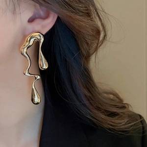 Close-up of golden liquid metal earrings with irregular design worn by a model