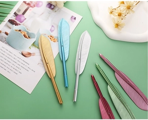 Flat lay of colorful metallic feather-shaped pens in six elegant finishes on a desk