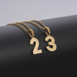 Détail macro de pendentifs chiffres 2 et 3 dorés sur de fines chaînes maillées