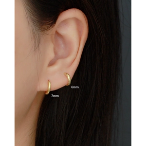 Detail of 6mm and 7mm gold huggie earrings shown on model ear for size scale