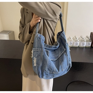 Détail du sac cabas en denim bleu avec texture délavée et bords effilochés à l'épaule