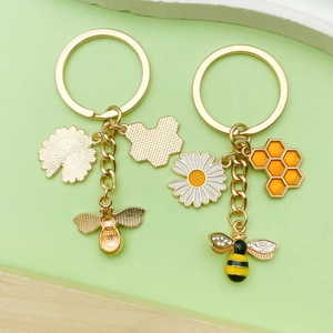 Detailed view of two bee keychains with honeycomb charms, daisies, and enamel finish