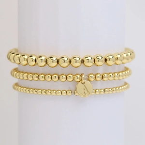 Three-piece set of golden beaded bracelets featuring a round initial A letter pendant tag