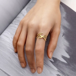 Close-up of a gold X-shaped interlocking ring on finger with polished metal texture