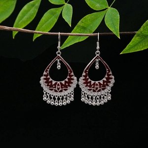 Macro detail of teardrop hollow ethnic earrings with silver beads and red enamel accents