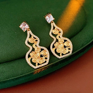 Macro shot of gold-plated hollow gourd earrings with shimmering crystals on green velvet