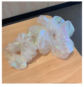 Detail shot of a white holographic organza scrunchie on a light wood surface