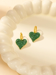 Elegant gold heart earrings with sparkling green crystals on a ceramic display