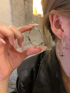 Detailed view of silver bow-accented hoop earrings held in hand and worn on ear