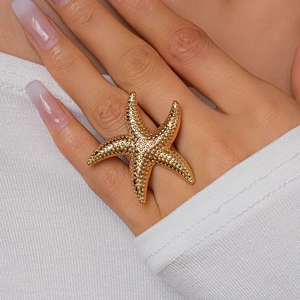 Detailed close-up of a large gold starfish ring with a textured finish on a model hand