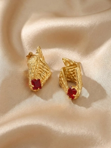 Detail of 18k gold plated conch earrings with red zircon and lava texture finish