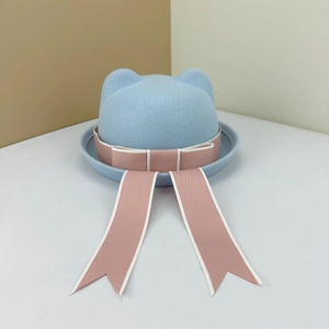 Close-up of a light blue wool felt cat-ear hat with a pink bow and trailing streamers.