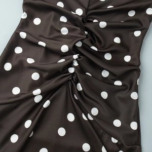 Détail macro du motif à pois et du nœud torsadé central sur la robe noire plissée