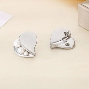 Detail view of silver heart earrings with three side-set pearls on polished steel surface