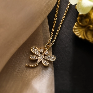 Golden dragonfly pendant necklace with sparkling cubic zirconia on luxury fabric background