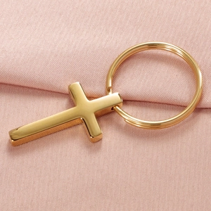 Polished golden stainless steel cross keychain with round ring on pink fabric background