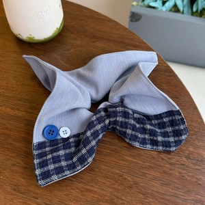 Close-up of blue and white plaid scrunchie with button accents on a wooden table