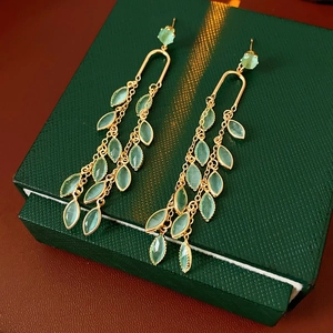 Détail de boucles d'oreilles feuilles dorées avec pierres vertes sur un coffret cadeau