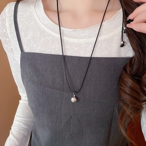Close-up of a silver hollow flower pendant on a black cord necklace worn by a model