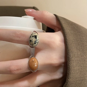 Detail of oval gemstone rings with brown amber and dalmatian stone on hand