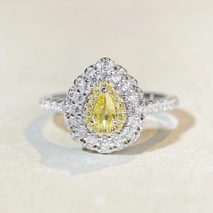 Macro view of pear-cut yellow gemstone ring with silver band and halo of clear stones