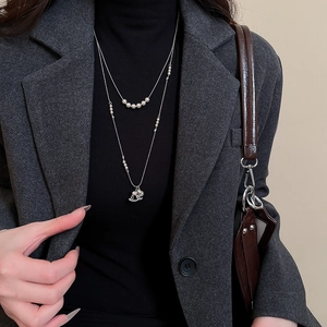 Close-up of layered silver necklace with pearl beads and a tiny rocking horse charm