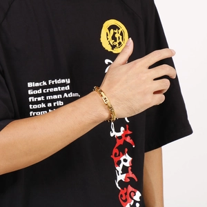 Detail of a gold-colored cuban link chain bracelet worn on a male model's wrist
