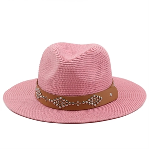 Detailed view of pink straw hat with brown leather band and silver flower rivets