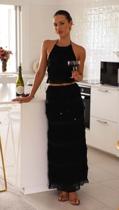 Detail of black halter crop top and layered chiffon maxi skirt on a model in a kitchen