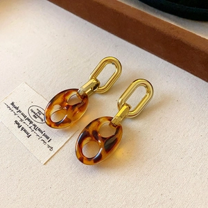 Macro shot of vintage style gold earrings with leopard pattern resin links on beige linen