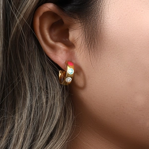 Detail of 18K gold C-shaped earrings with colorful enamel smiley face icons on model