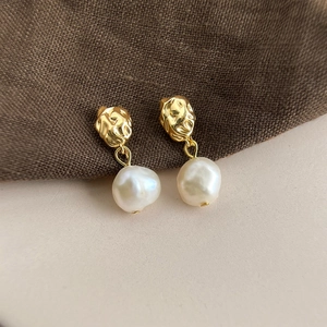 Close-up of baroque pearl earrings with hammered gold metal texture in a vintage style